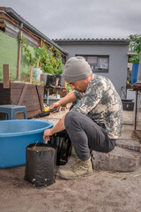 Caucasian male putting soil in black garden pots for gardening with his Jack Russell Terrier dog, Cape Town, South Africa