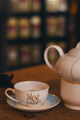 A picture of a white porcelain cup and teapot with flower motives, positioned neatly on a wooden table 