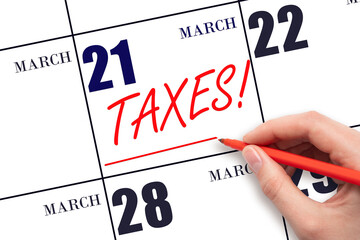 Hand drawing red line and writing the text Taxes on calendar date March 21. Remind date of tax payment