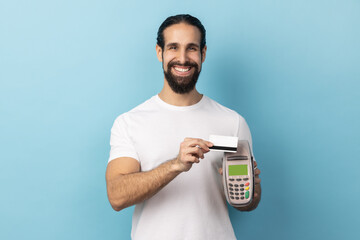 Portrait of smiling man with beard wearing white T-shirt holding in hand pos payment terminal,...