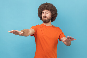 Portrait of man with Afro hairstyle moving with closed eyes, touching space with hands, confused...