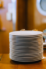 A pile of white clean round empty plates stand in a row on a wooden kitchen table.