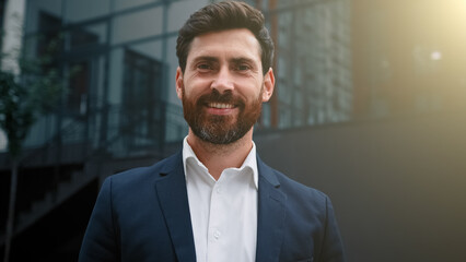 Fototapeta premium Elegant successful caucasian businessman wearing formal suit happy male portrait of adult 30s employee bearded middle eastern attractive man posing outdoors modern city office background in sunny day
