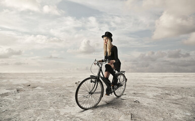 young woman with top hat travels by bicycle in the middle of a desert