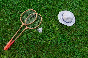Badminton rackets, a shuttlecock and a hat lie on a green lawn. The concept of active recreation, outdoor games.Top view
