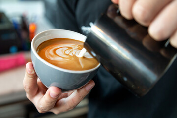 Barista preparing cafe latte, pouring milk into a coffee. Closeup on male hands with latte art.