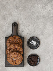 Chocolate brownie cookies with sea salt fleur de sel served on a wooden board. Ingredients on a...