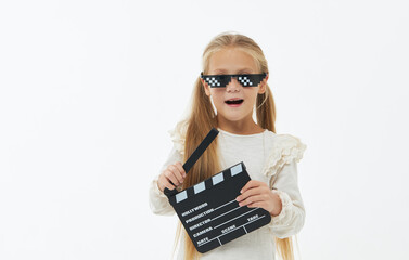 Funny smiling child girl in cool eyeglasses hold film making clapperboard isolated on white background. Studio portrait. Childhood lifestyle concept. Copy space for text