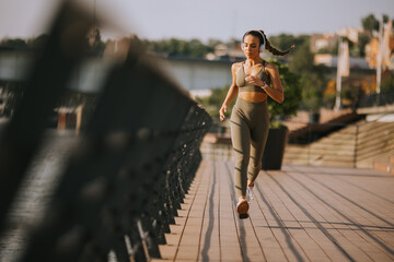 Active young beautiful woman running on the promenade along the riverside