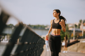 Active young beautiful woman running on the promenade along the riverside