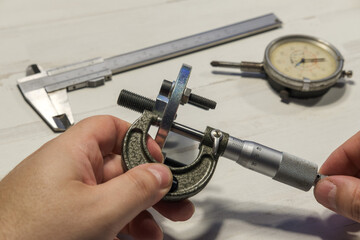 Manos de mecánico midiendo de espesores con micrómetro donde se aprecian además un calibre pie...
