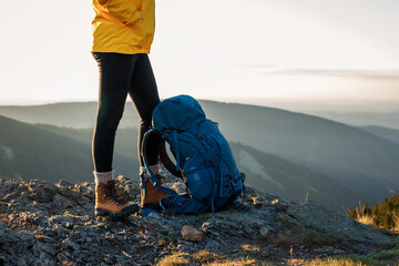 Woman with backpack and hiking boot standing on rock after climbing to mountain peak. Trekking outdoors - obrazy, fototapety, plakaty