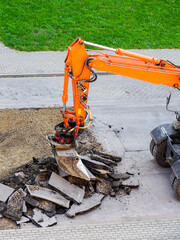 An excavator breaks up the old asphalt layer with a bucket during street repairs
