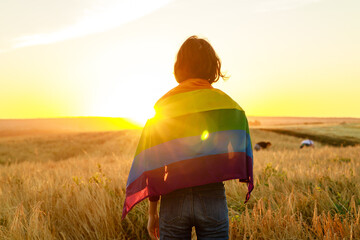 woman in field holding rainbow lgbt flag in golden sunset evening sunshine