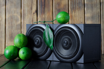 Two wooden audio speakers - speaker system next to fresh green limes. Background from natural pine...