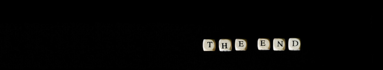 The inscription The end on wooden cubes on a black background. Tragedy, pessimism, ending and fate. Web banner. Copy space.