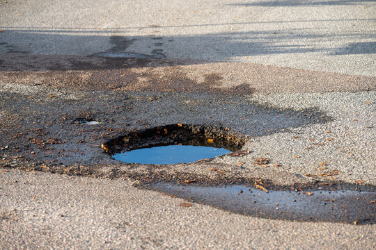 A dep pothole in asphalt parking lot filled with water.