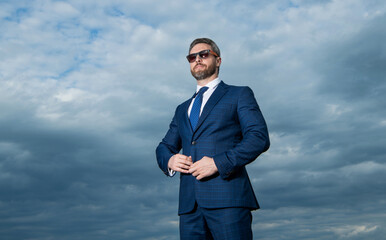 Professional guy sky background. Grizzled guy wearing sunglasses. Serious guy buttoning suit jacket