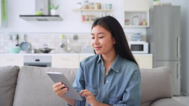 Young casual asian woman entrepreneur using digital tablet relaxing at home
