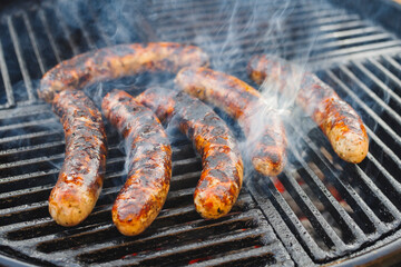 Gegrillte Allgäuer Bratwurst angeboten als close-up auf einem Holzkohlegrill mit Feuer und Rauch