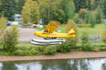 Yellow bush float plane flying over river in Alaska