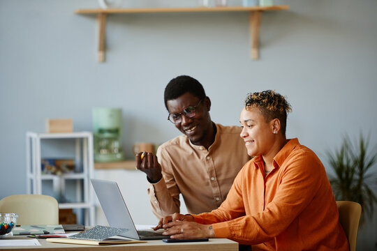 Side view portrait of two black business people using laptop together and smiling while working on project in office, copy space