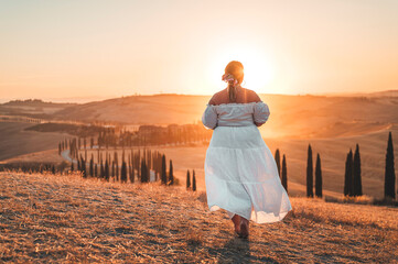 Woman wearing white admiring a sunset over Tuscan hills during sunset and holden hour 