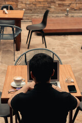 Back of an unrecognizable person working with a computer, in a coffee shop.