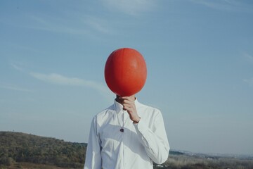 Person holding a red balloon in front of his face - Powered by Adobe
