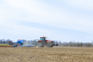 Obraz premium Agricultural tractor sows seeds in the field. Seeding equipment is working on the farmer's field.