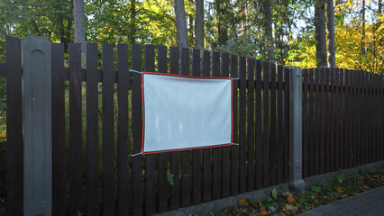 White empty banner with mockup space in red frame mounted on wooden fence outside