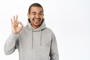 Excellent, good choice. Smiling handsome guy shows okay, ok sign, recommending smth great, complimenting, standing over white background