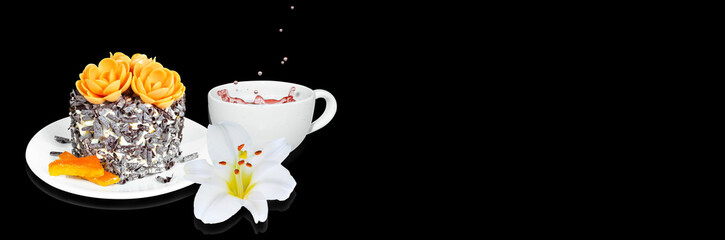 A small cake with candied orange and chocolate chips, a cup of tea and a flower on a black widescreen background. Selective focus, banner