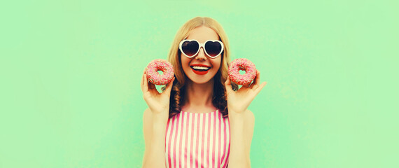 Portrait of happy cheerful laughing young woman with two donuts having fun on green background