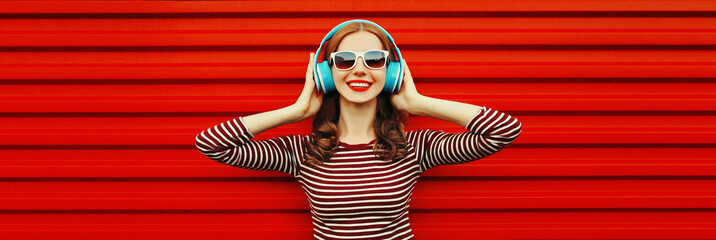 Portrait of happy smiling young woman with headphones listening to music on red background