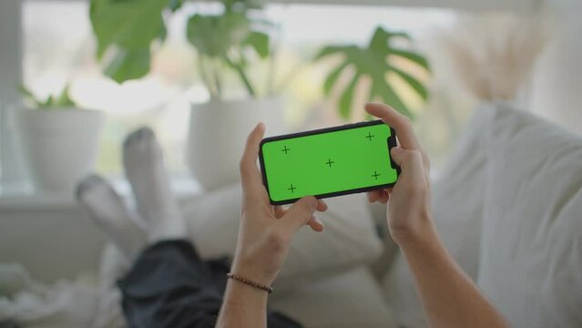 Man laying on couch, playing game on iphone, mockup, green screen