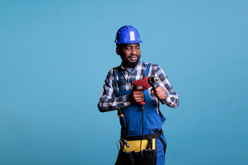 Studio portrait of african american worker in overalls work uniform safety helmet holding cordless screwdriver. Construction contractor doing renovation of house interior.
