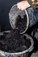 A man pours coal into a bucket. Fuel for heating a private house