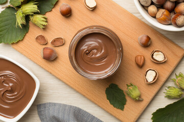 Hazelnut cream with nuts and green leaves on wooden background, top view