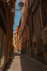 Fototapeta na wymiar Beautiful narrow street with vintage houses buildings and an old man walking in Italy. Traveling in Europe with ancient architecture in sunlight and shadow