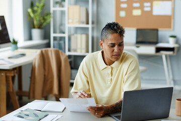 Fototapeta premium Portrait of tattooed African American woman using laptop at office workplace and wearing casual clothes