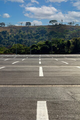 Big parking lot completely empty with hill covered by vegetation in the background. Vertical