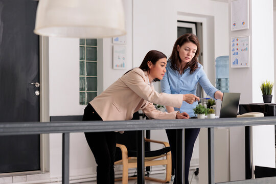 Employees collaboration, coworkers discussing company report in coworking space, woman pointing at computer screen. Workers chatting about strategy plan, standing in office