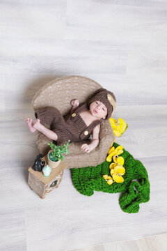 cute infant boy wearing brown knitted dress with head cap lying at tiny chair,face photography,props
