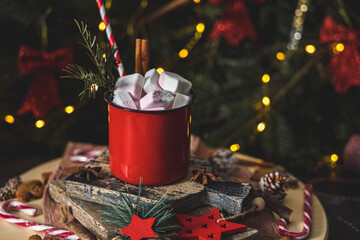 One red iron mug with hot cocoa, marshmallows on top with cinnamon, gingerbread man on cutting board .