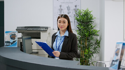 Portrait of asian receptionist working with medical checkup papers and appointment reports at...