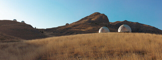 Modern glamorous camping in the autumn mountains of Dagestan. A group of futuristic hotel geodesic domes tents in the middle of a dry grass meadow in the Khunzakh region. - obrazy, fototapety, plakaty