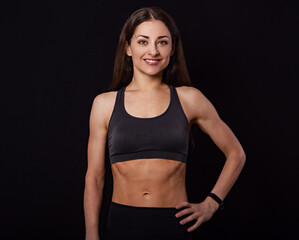 Fototapeta na wymiar Confident sportswoman in grey sportsbra and shirt, holding hands on waist, fitness trainer standing in power pose, workout in gym isolated on black background
