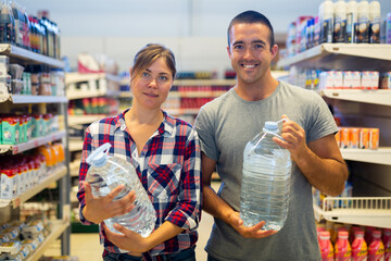 Portrait of positive couple holding bottles of water in supermarket. Wife and husband shopping in grocery store.