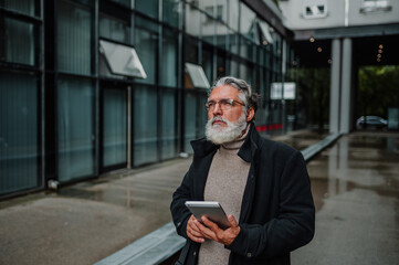 Portrait of a senior businessman using tablet outside of the office building